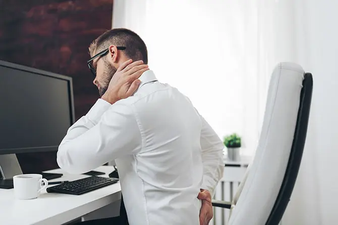 Office worker with neck pain from prolonged computer work on his work desk.