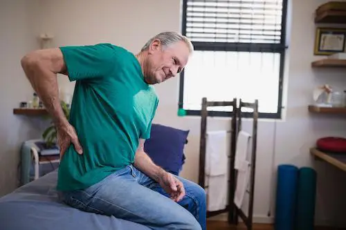 Elderly man sitting on his bed and experiencing back pain.