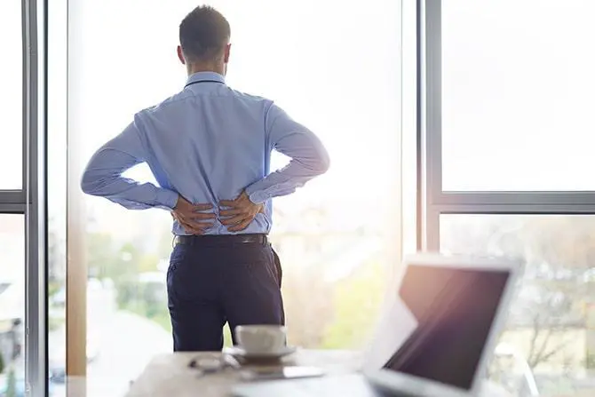 Back view of a business man holding his lower back because of back pain.