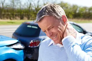 auto accident victim holding his painful neck with his car bumping into another car in the background