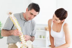 Male chiropractor shows female patient portion spine to explain sciatica pain