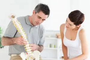 Male chiropractor shows female patient portion spine to explain sciatica pain