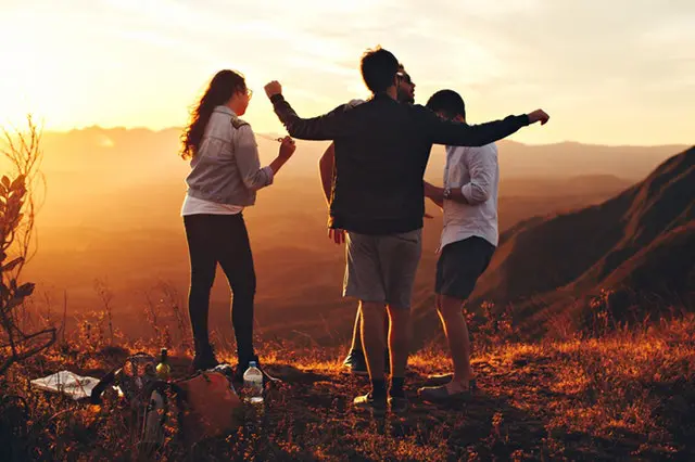 Four young people standing on top of a grassy mountain and having fun.