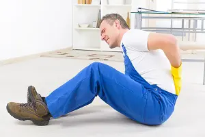 Man crouching on the floor holding his back due to personal injury.