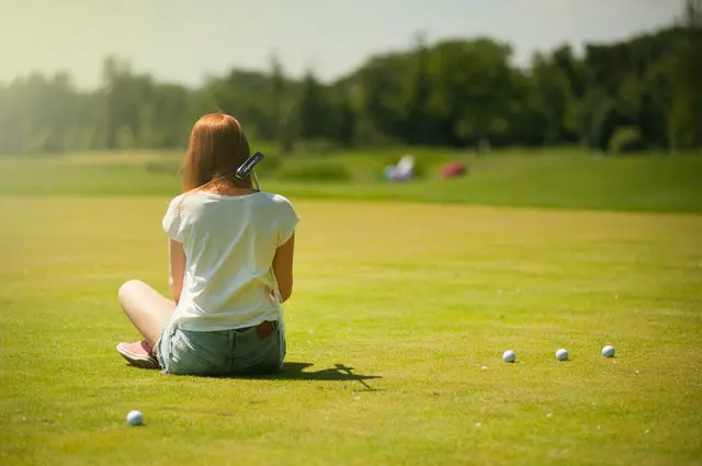 Woman sitting on a grass field of a golf course with golf balls around her.