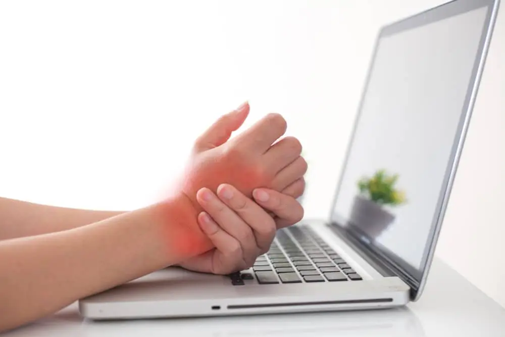 Person in front of laptop holding his wrist due to pain.