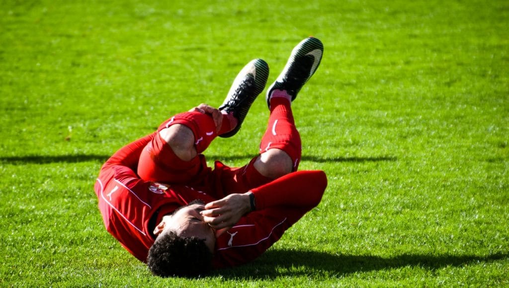 Soccer player crouching in pain due to sports injury. Treatment available at Hogan Spine & Rehab