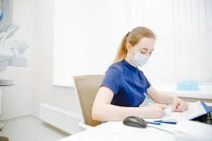 Woman in blue neck t-shirt writing, scheduling new patient appointments at Hogan Spine & Rehab