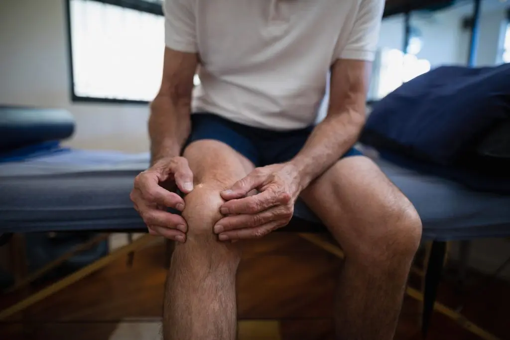 Male patient holding the midsection of his knee due to knee pain.