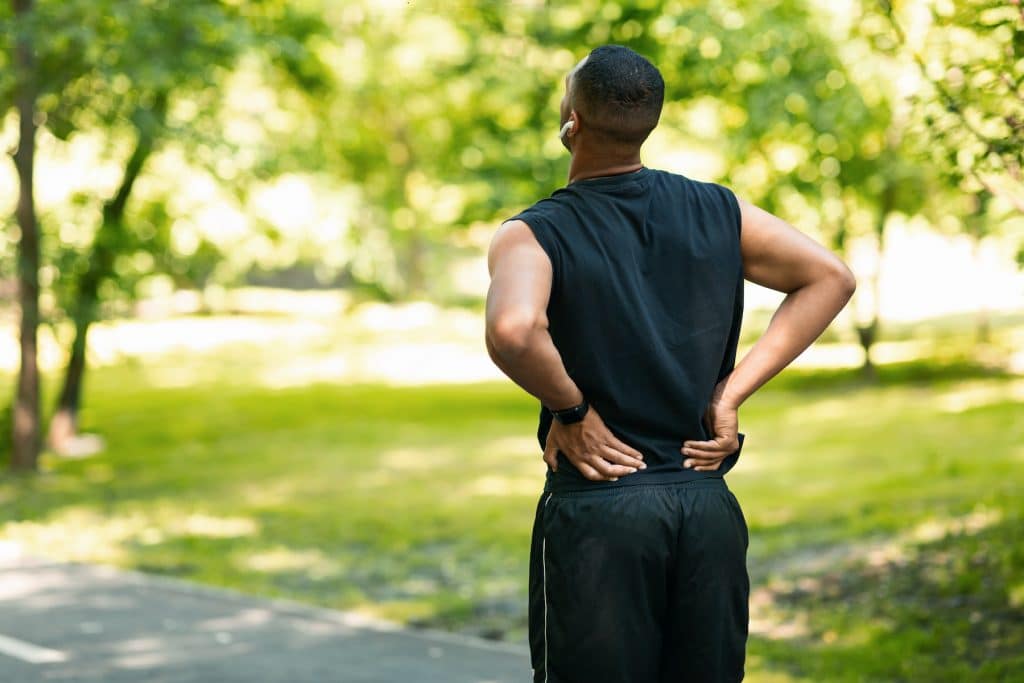 Millennial guy in sportswear suffering from back pain.