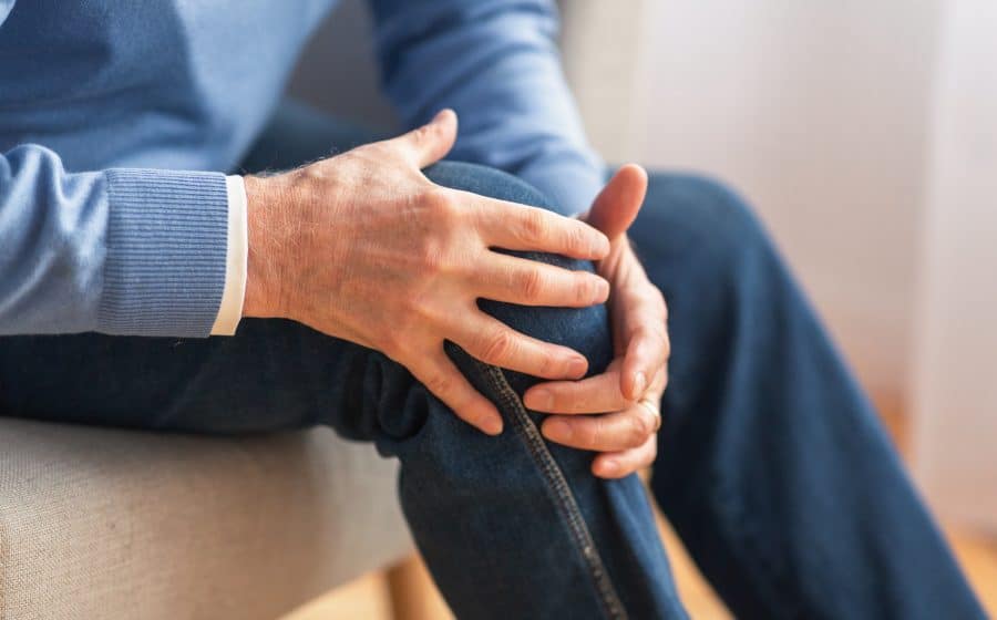 Senior man sitting on a sofa massaging his knee due to pain.