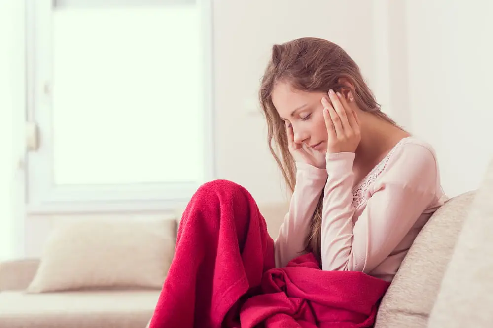 Young lady massaging her head while sitting on a couch due to headache.