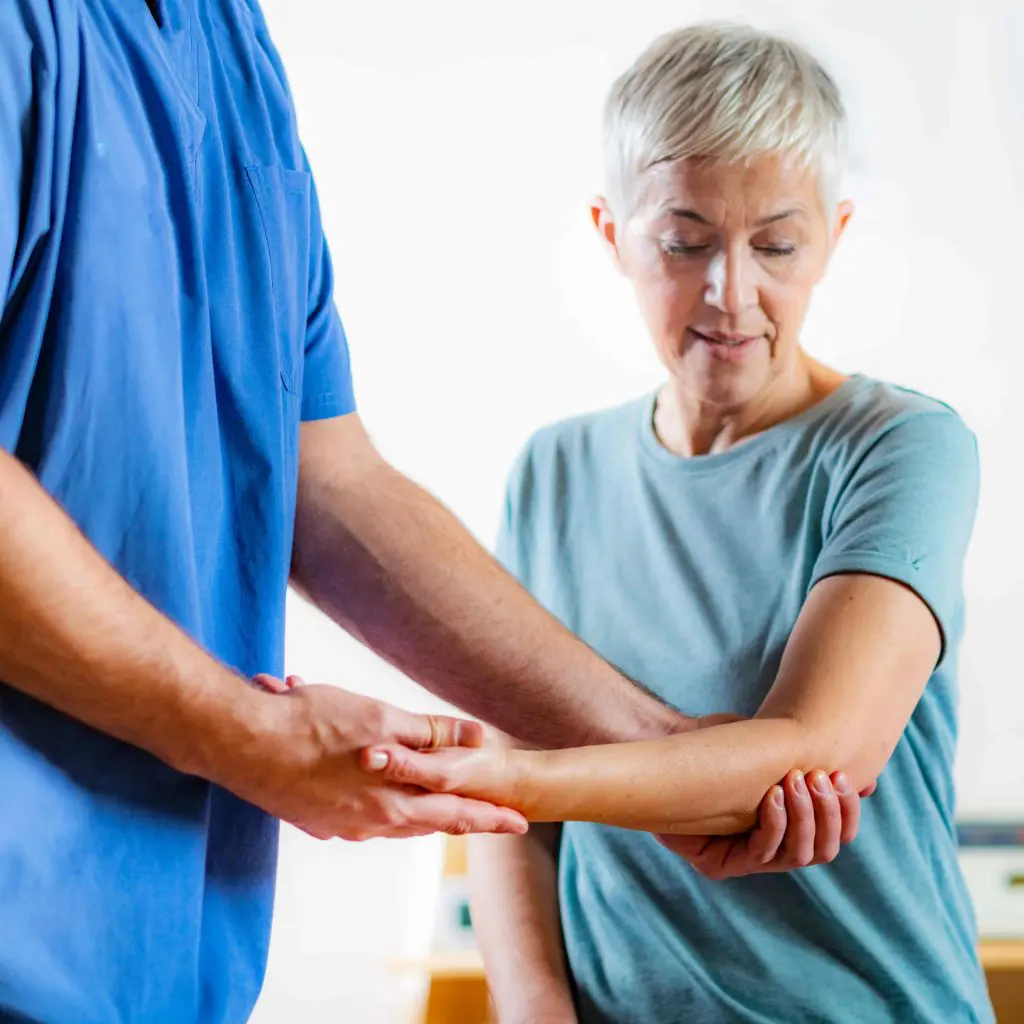 Chiropractor holding an elderly patient's arms while post surgery physical therapy.