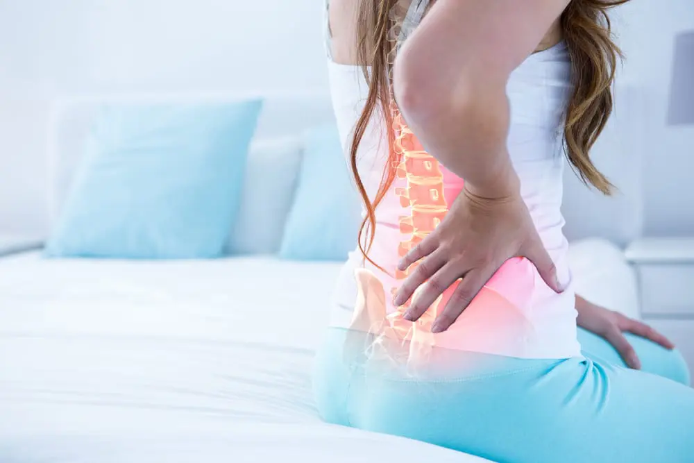 Woman sitting on her bed while supporting her back to pain cause by scoliosis