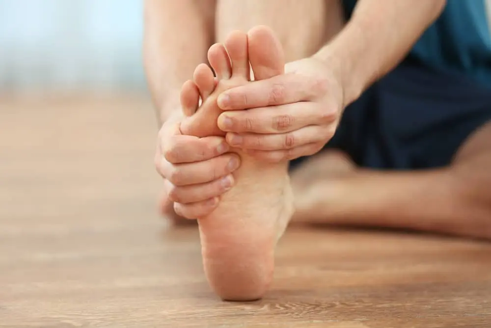 Man sitting on the floor holding his foot due to pain caused by plantar fasciitis. 