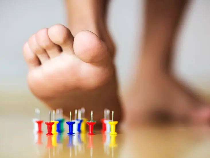Close up of a man's foot about to step on push pins to illustrate the pain caused by plantar fasciitis.