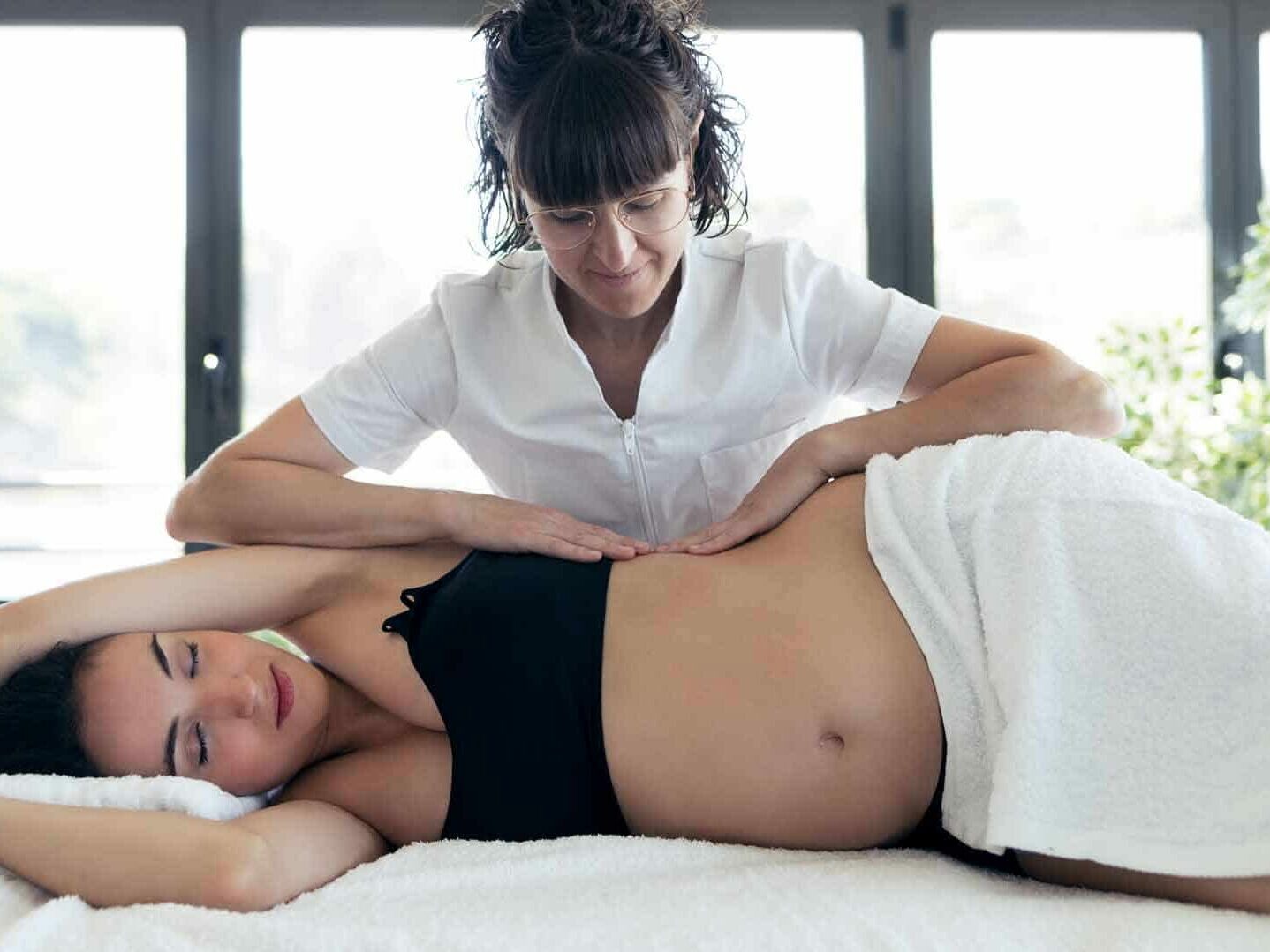 therapist doing belly massage to beautiful pregnant woman