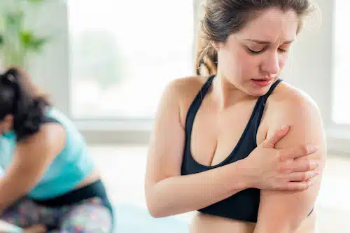 woman at the gym experiencing sharp stabbing pain on her shoulder