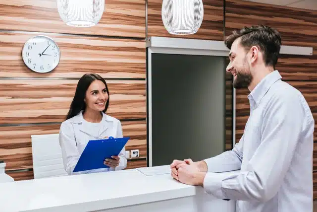 Female receptionist helping the patient with his paper works in a chiropractic clinic 